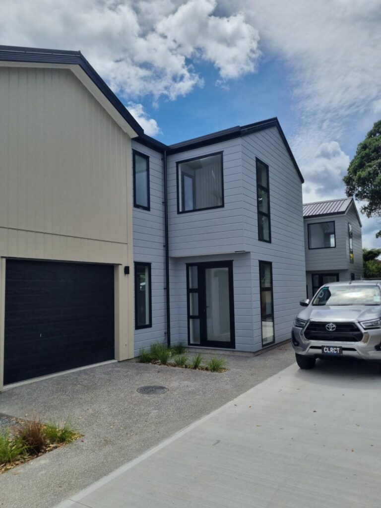Contemporary two-storey new build home in Wellington with grey cladding, black window frames, and attached garage, showcasing modern architecture and quality construction.